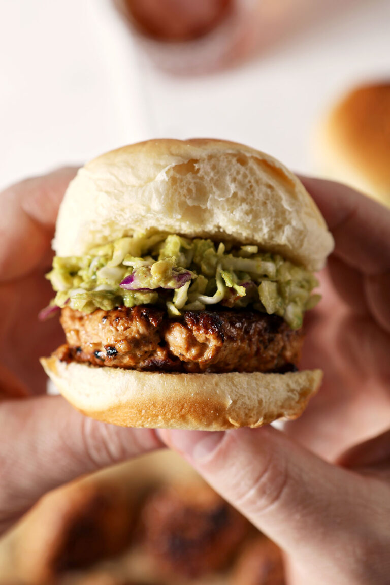 Hands hold a BBQ Chicken Slider with Avocado Slaw above a marble surface