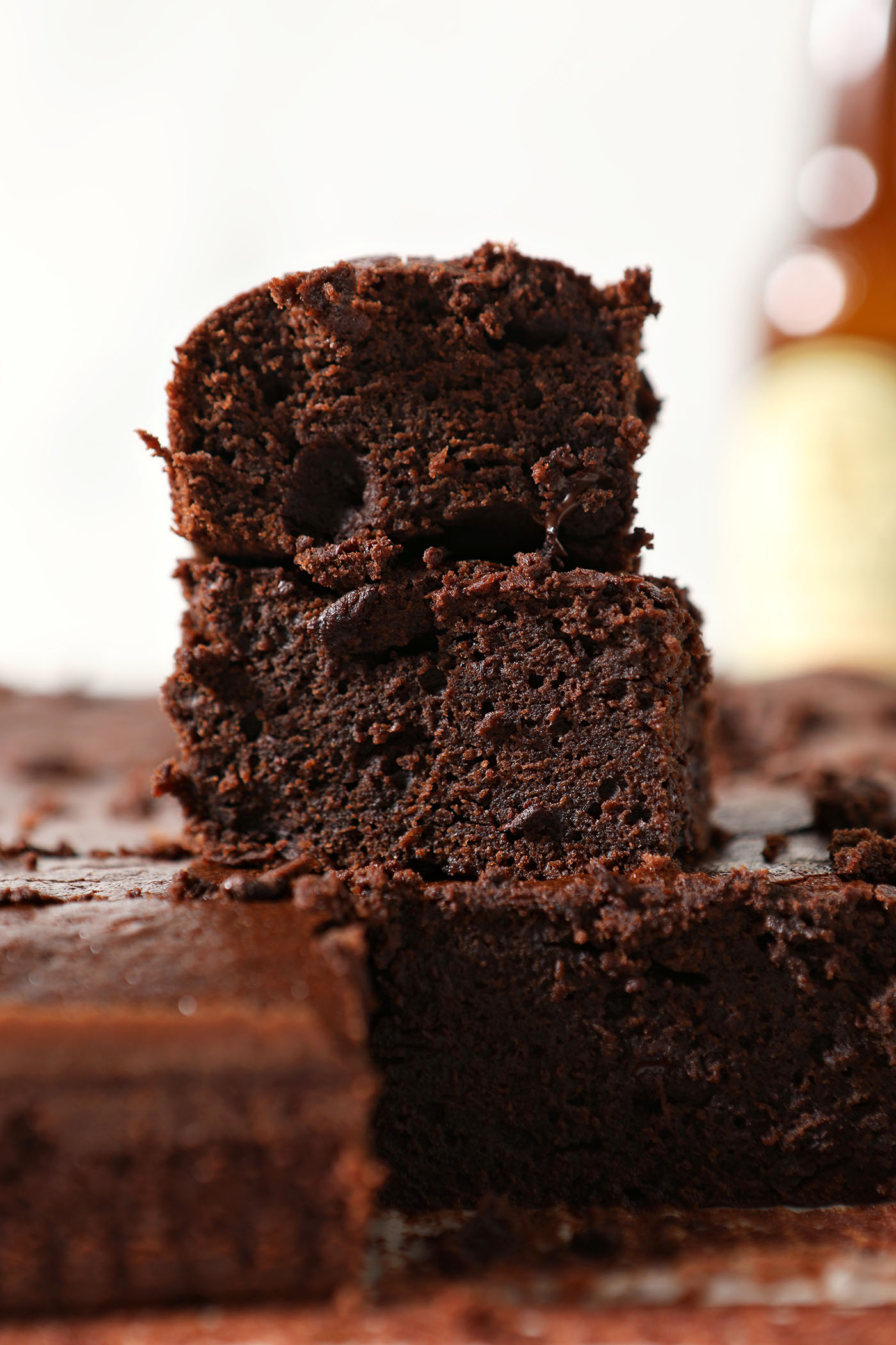 Gooey brownies stacked on top of each other in front of a beer bottle