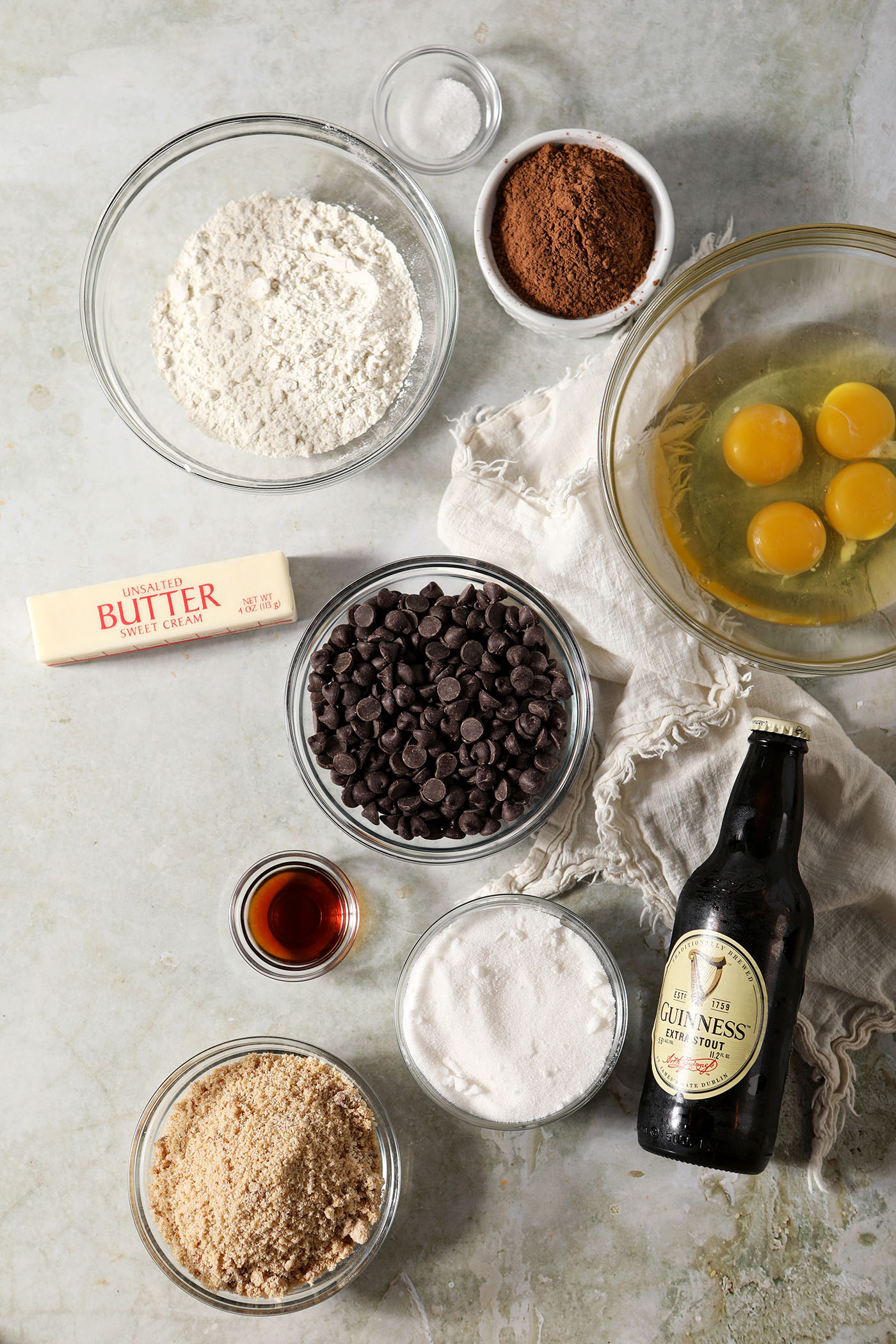 Ingredients to make Guinness stout brownies in bowls on a light green surface with a cream-colored linen