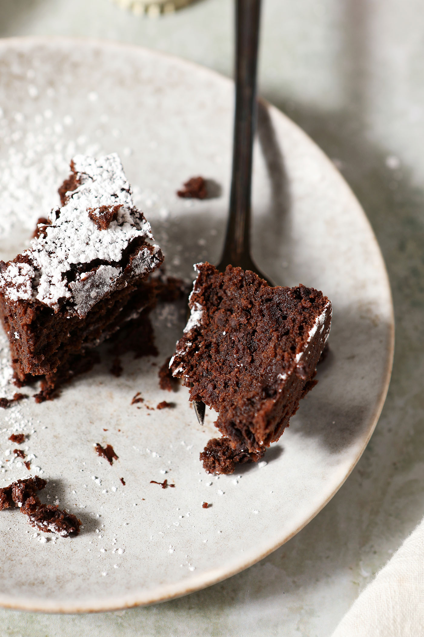 Close up of a fork holding a bite of a Guinness brownie on a grey plate on a light green surface