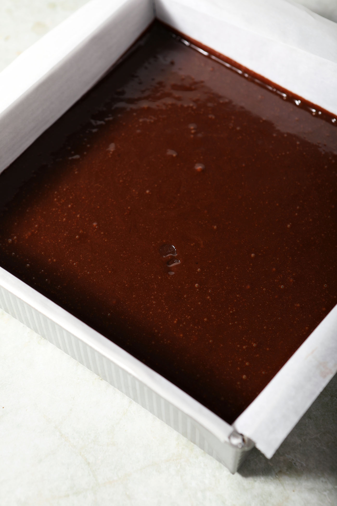 Brownie batter in a square pan before baking on a green surface