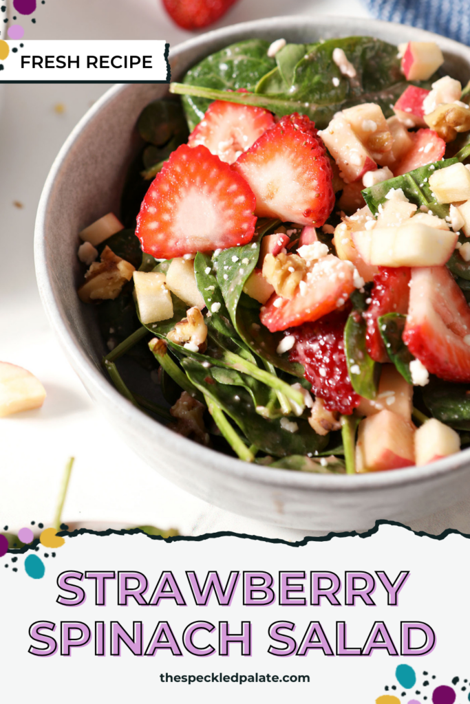 Close up of a bowl of strawberry salad with spinach, apples, nuts and feta on marble next to a blue linen with the text strawberry spinach salad