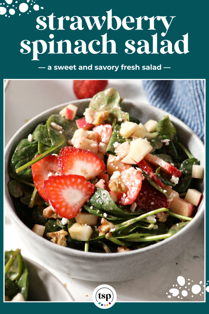 Close up of a bowl of strawberry salad with spinach, apples, nuts and feta on marble next to a blue linen with the text strawberry spinach salad a sweet and savory fresh salad