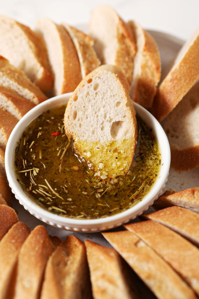 A piece of bread dunked into a parmesan spice olive oil dipping sauce surrounded by more slices of bread