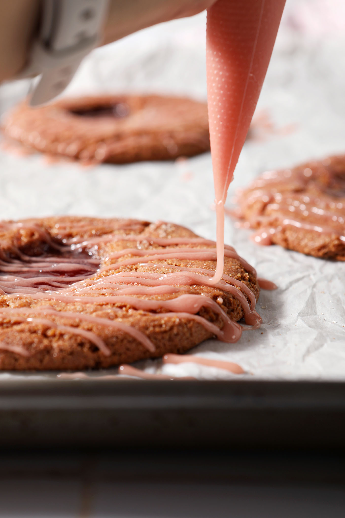 Icing drizzles onto a strawberry lemon cookie on a sheet pan