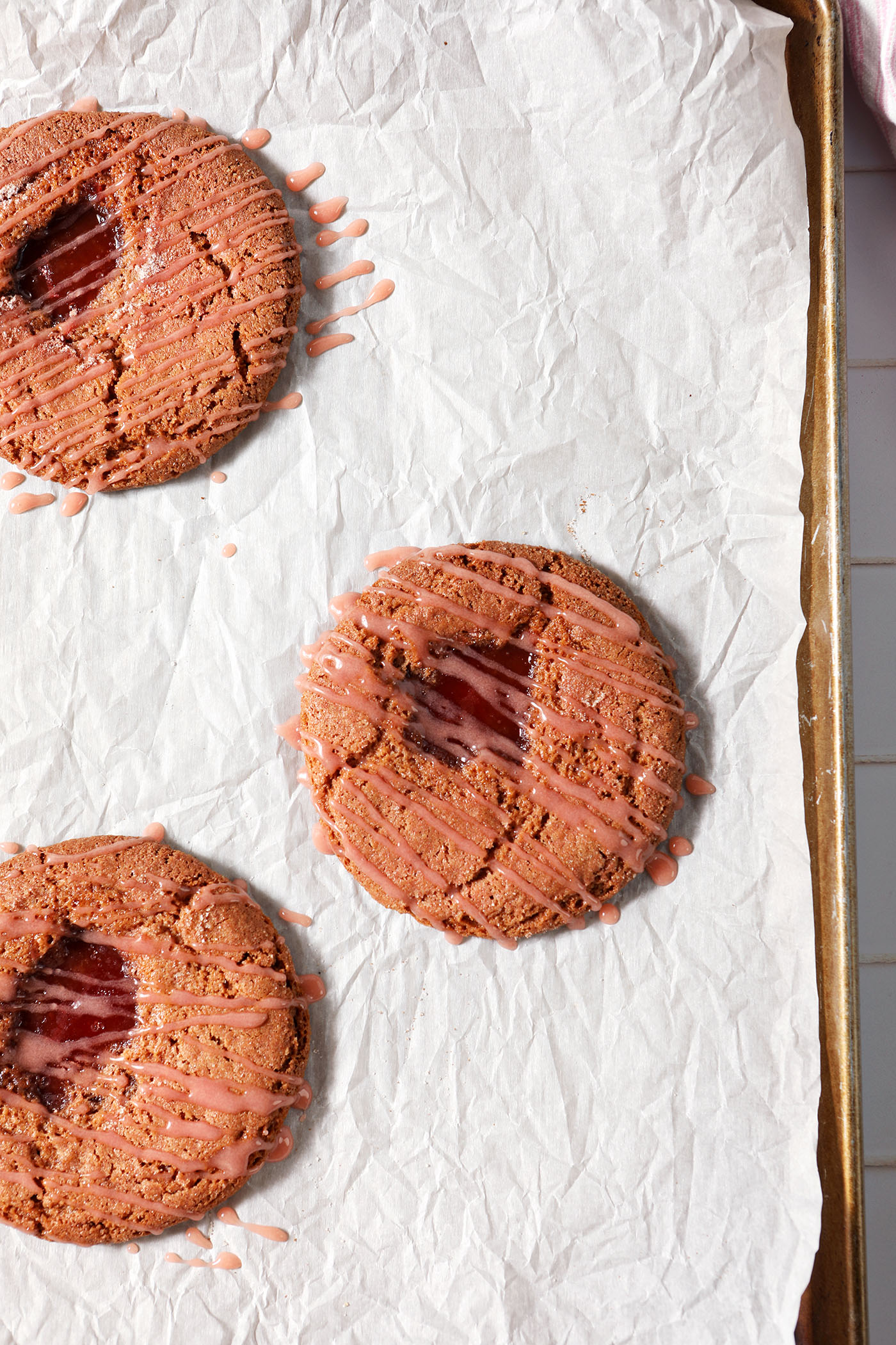 Overhead of three Strawberry Lemonade Cookies on a cookie sheet after baking and frosting
