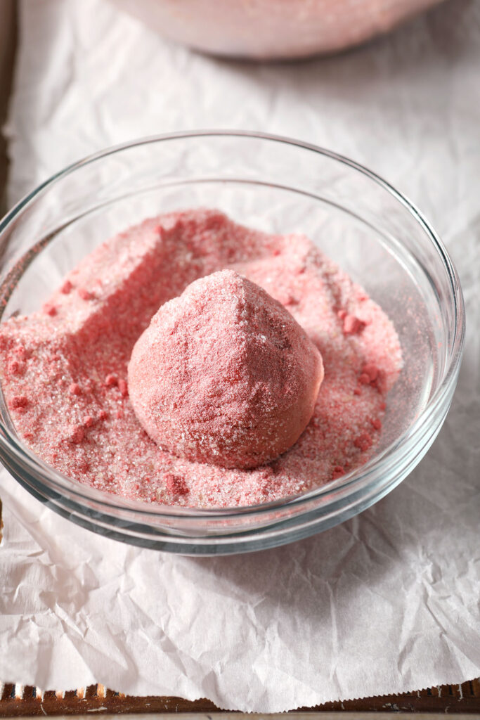A Strawberry Lemonade Cookie dough ball rolls in strawberry sugar