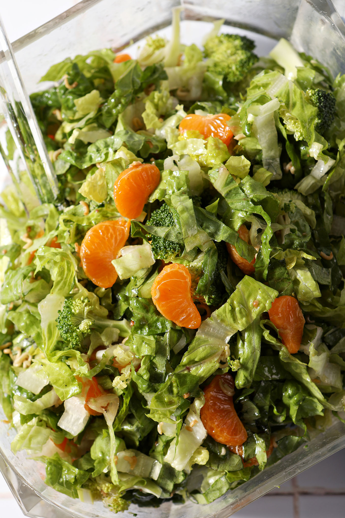 Close up of a large glass salad bowl holding ramen noodle, clementine and broccoli salad