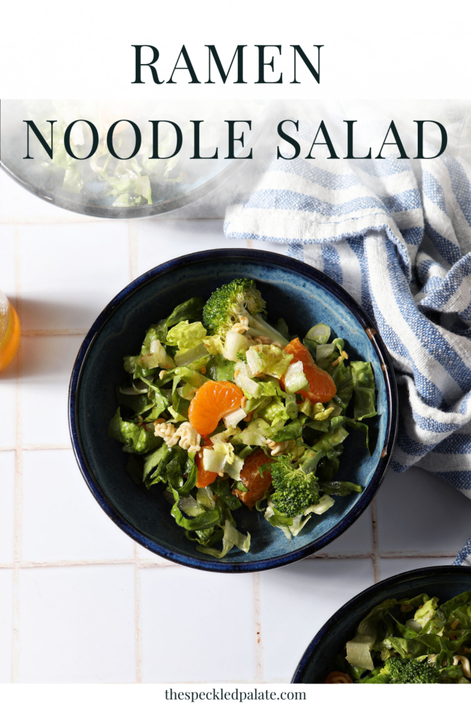 Three blue bowls holding clementine ramen noodle salad with broccoli on a white tiled surface next to a blue and white linen with the text ramen noodle salad
