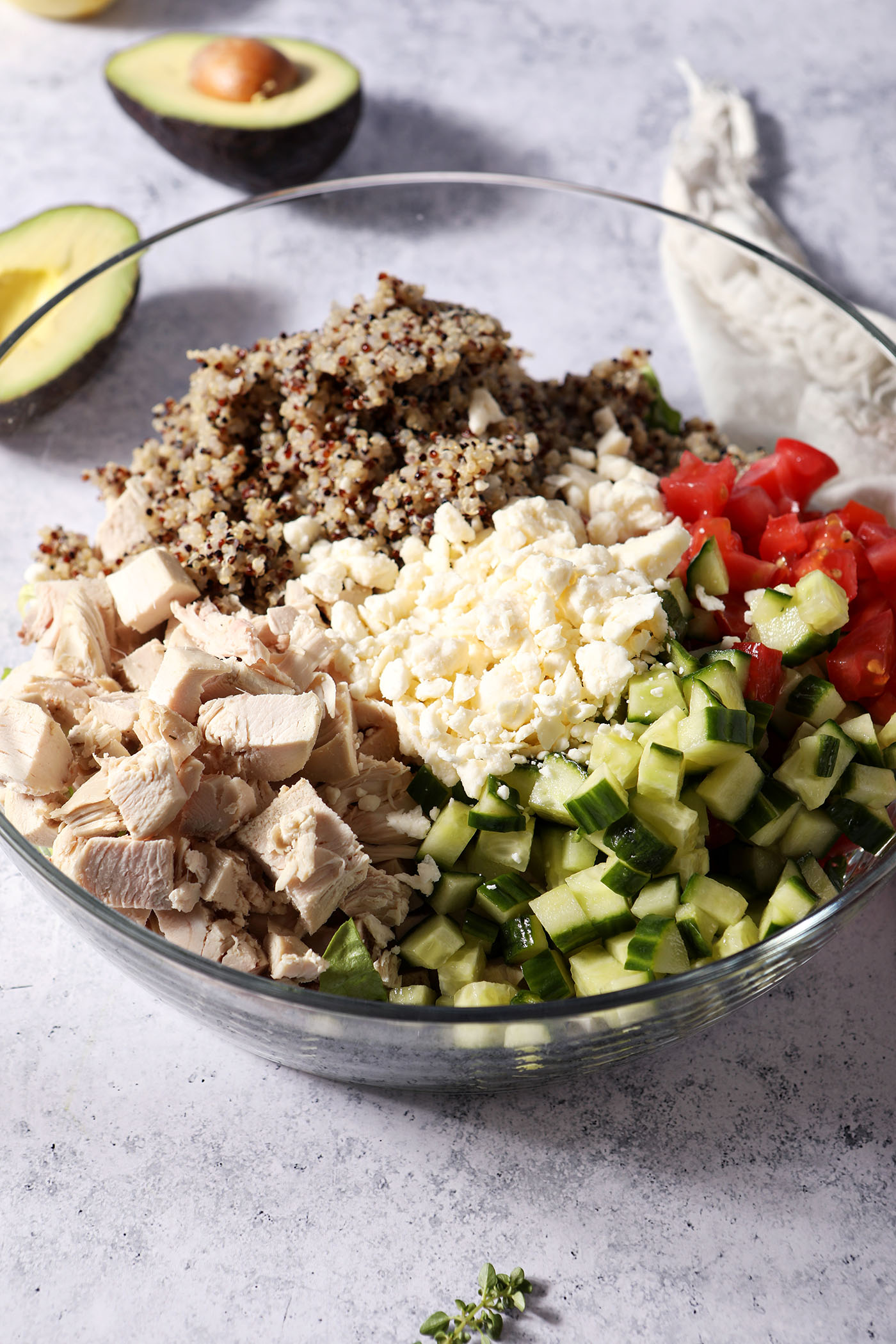 Ingredients to make lemon quinoa salad in a bowl before mixing in front of halved avocados