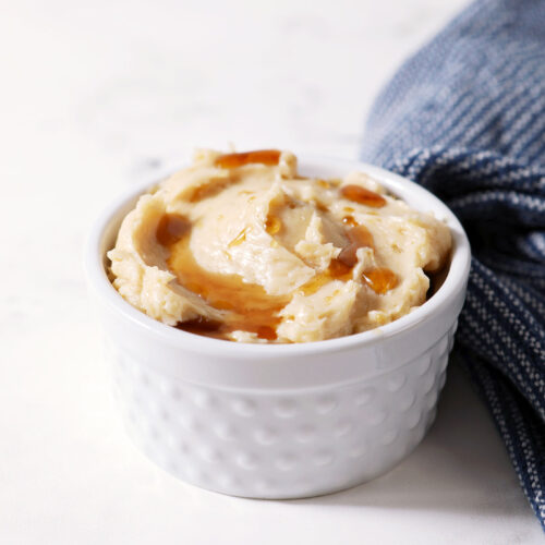 A ramekin of maple butter drizzled with extra maple syrup next to a blue linen