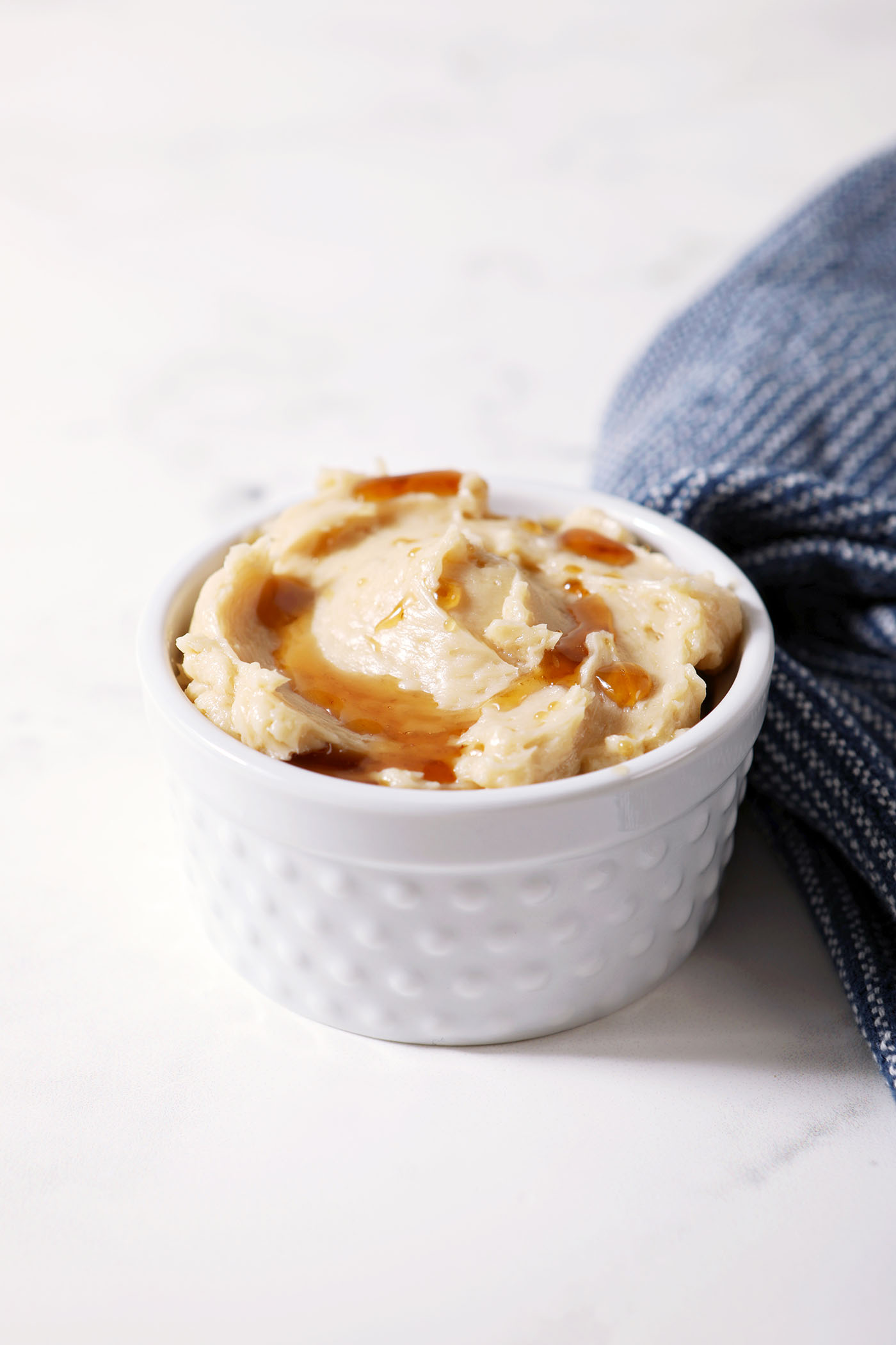 A ramekin of maple butter drizzled with extra maple syrup next to a blue linen