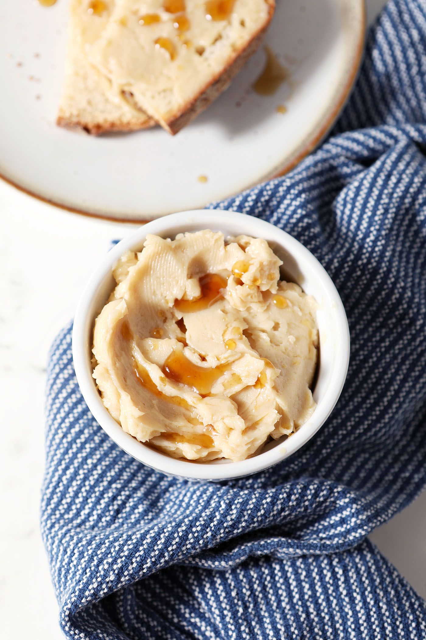 Overhead of a ramekin of maple butter drizzled with extra maple syrup next to a slice of bread with butter and a blue linen