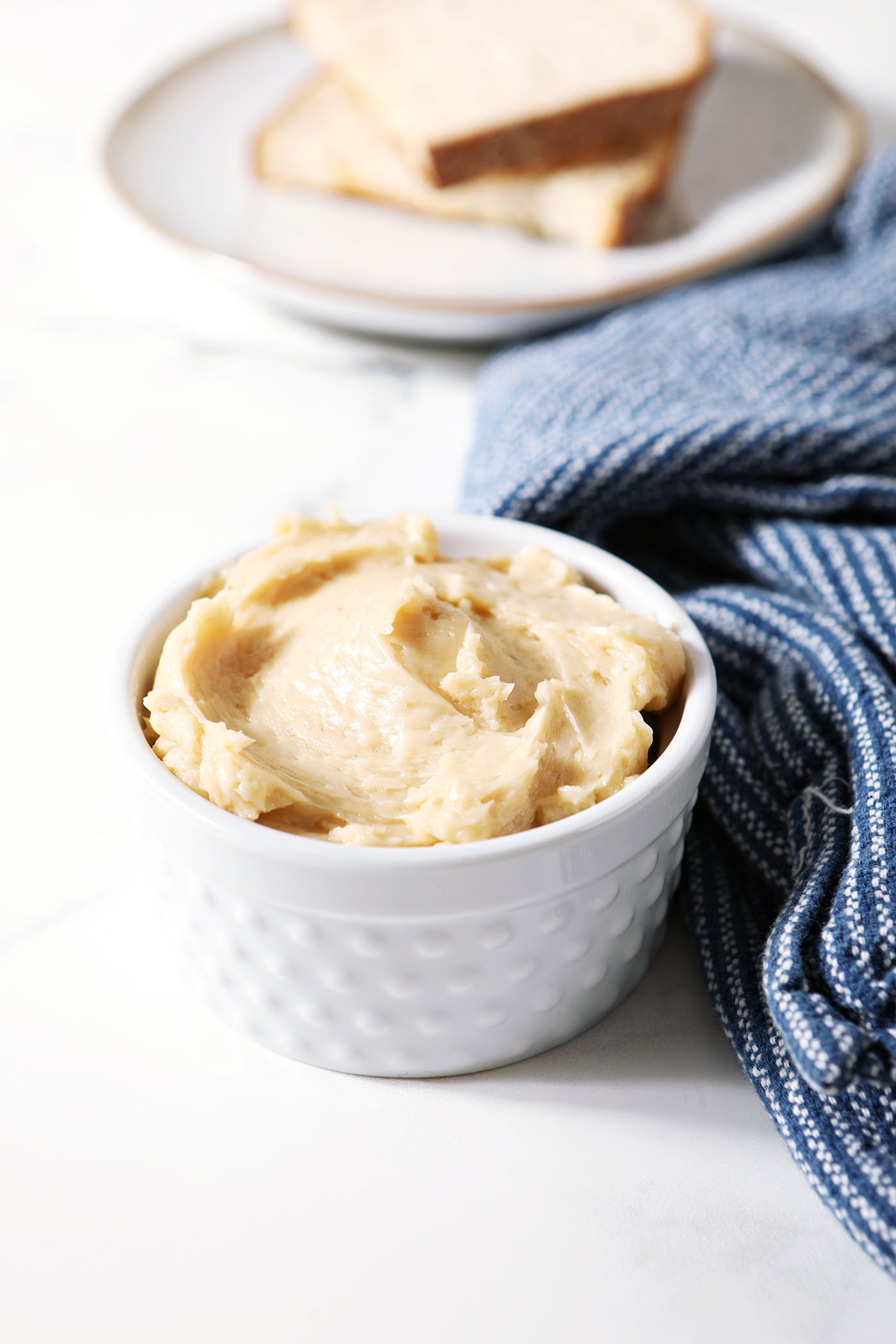 A ramekin of maple compound butter in front of a plate of toast and next to a blue linen