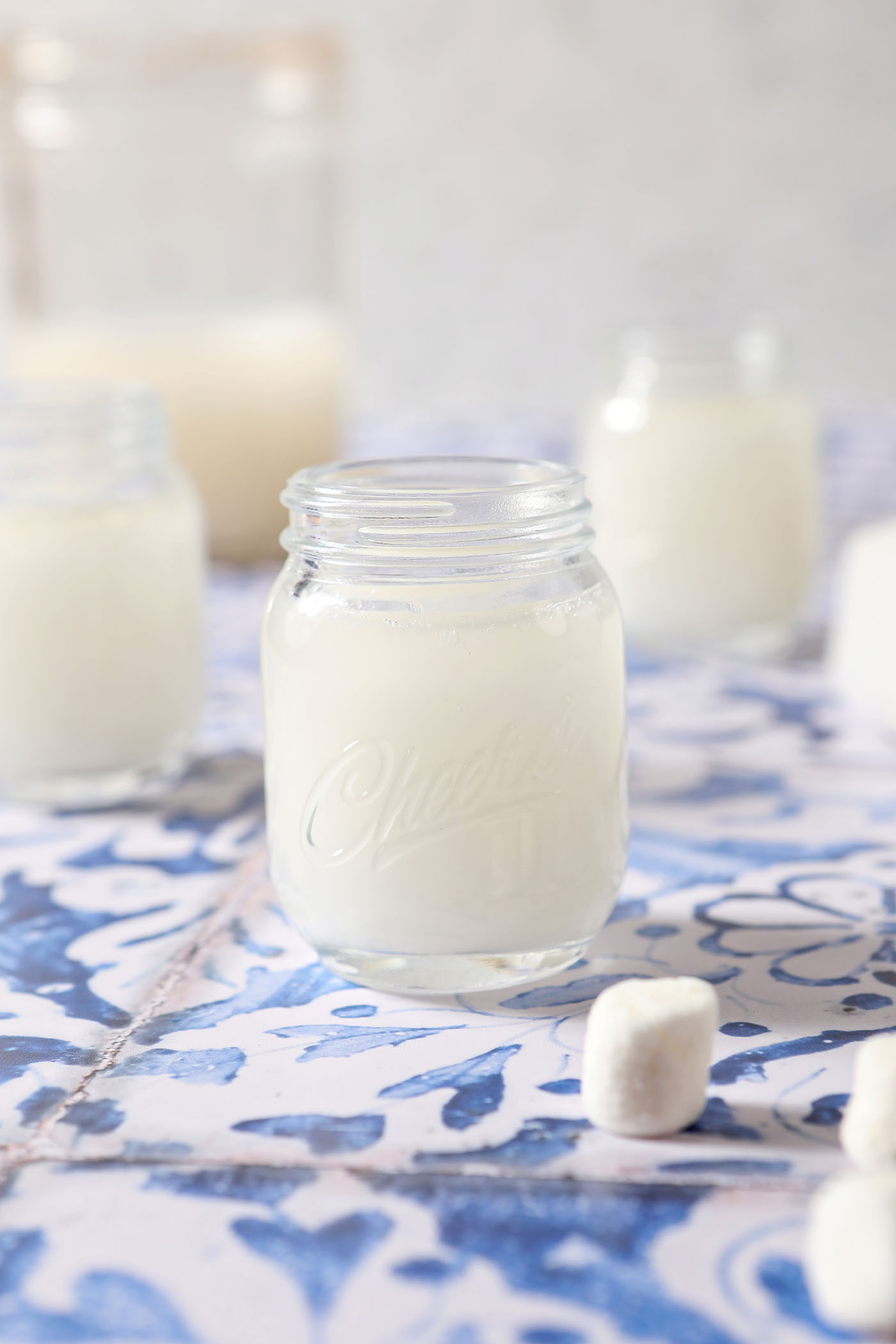Two shot glasses of marshmallow vodka on a blue and white tiled surface