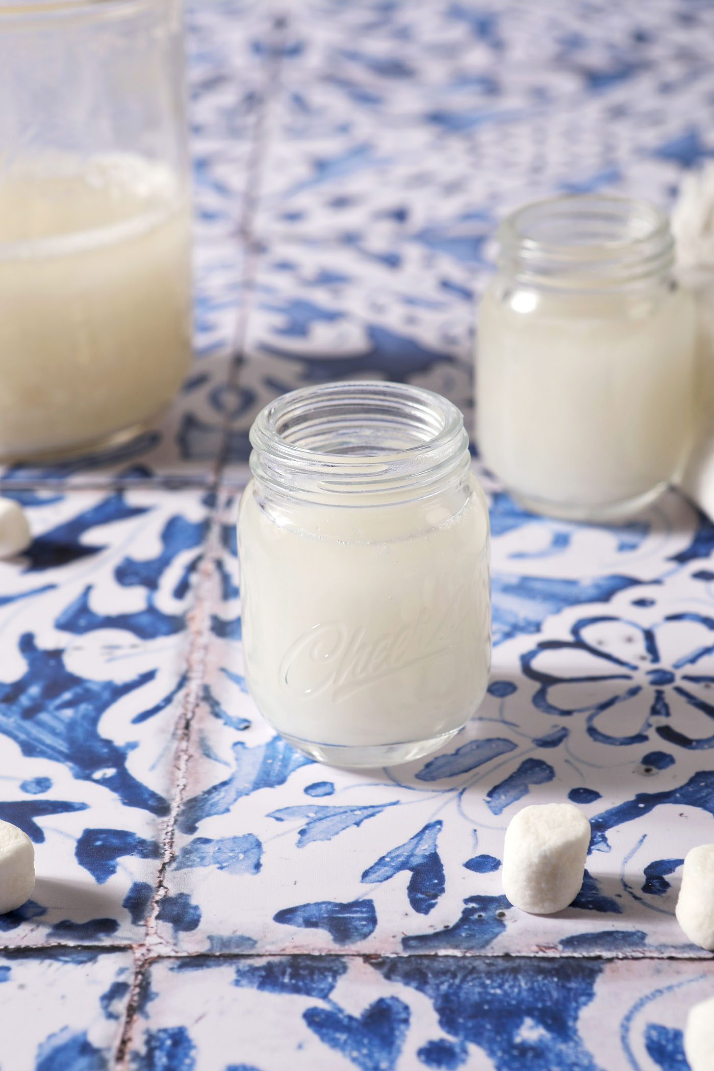 Two shot glasses of marshmallow vodka next to a mason jar of additional infused vodka