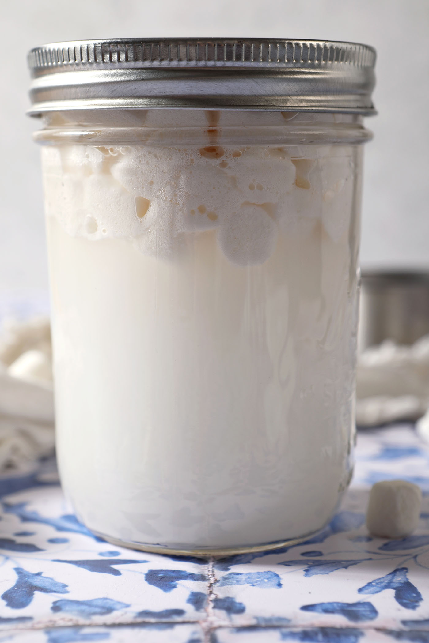 Love the flavors of marshmallow as a part of your drinks? This homemade Marshmallow Vodka is an easy infused alcohol to make at home and tastes like those classic marshmallows we all know and love. All you need are two ingredients and a little time.
Side angle of marshmallow vodka as it infuses on a blue and white tiled surface