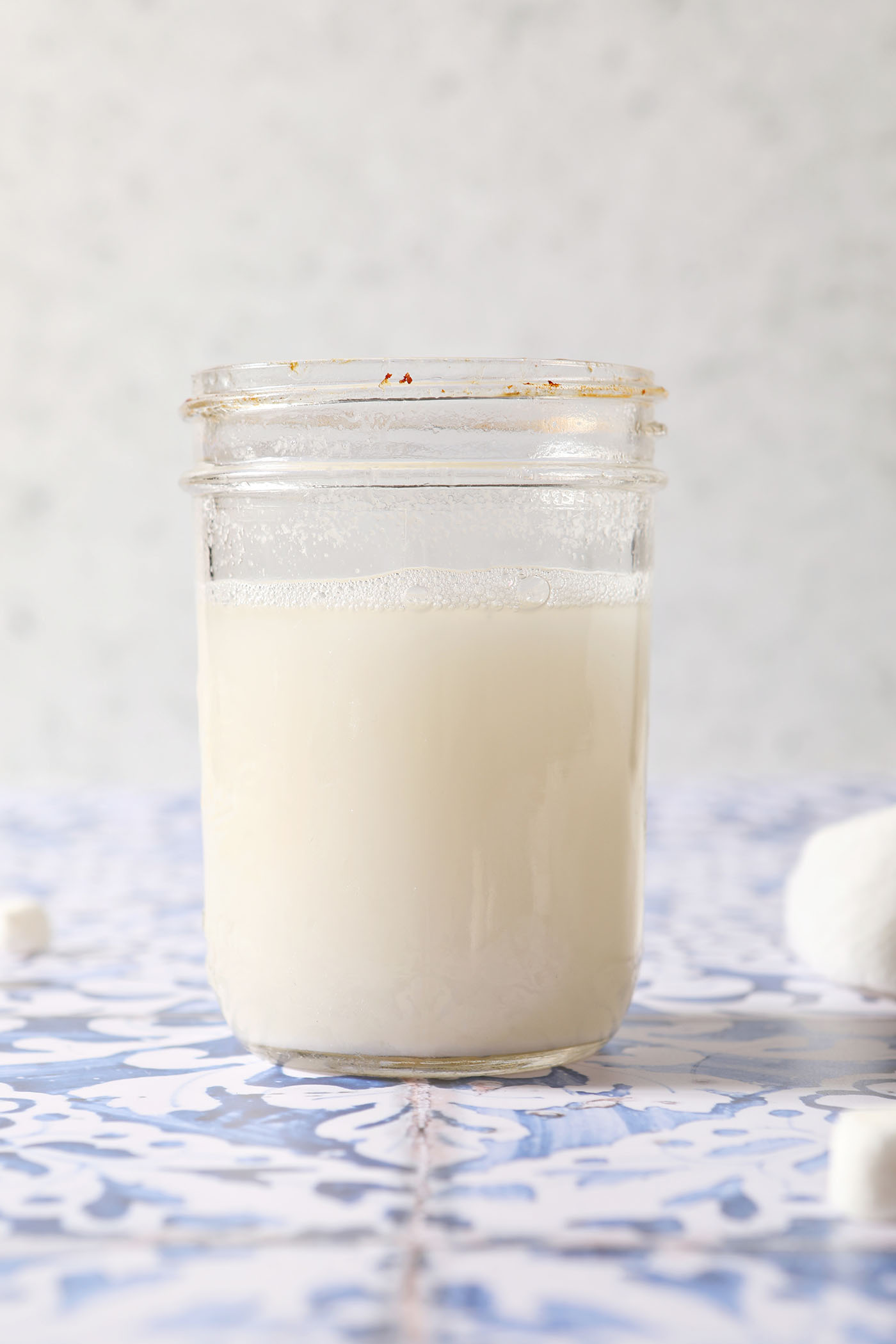 Love the flavors of marshmallow as a part of your drinks? This homemade Marshmallow Vodka is an easy infused alcohol to make at home and tastes like those classic marshmallows we all know and love. All you need are two ingredients and a little time.
Infused marshmallow vodka on a blue and white tiled surface
