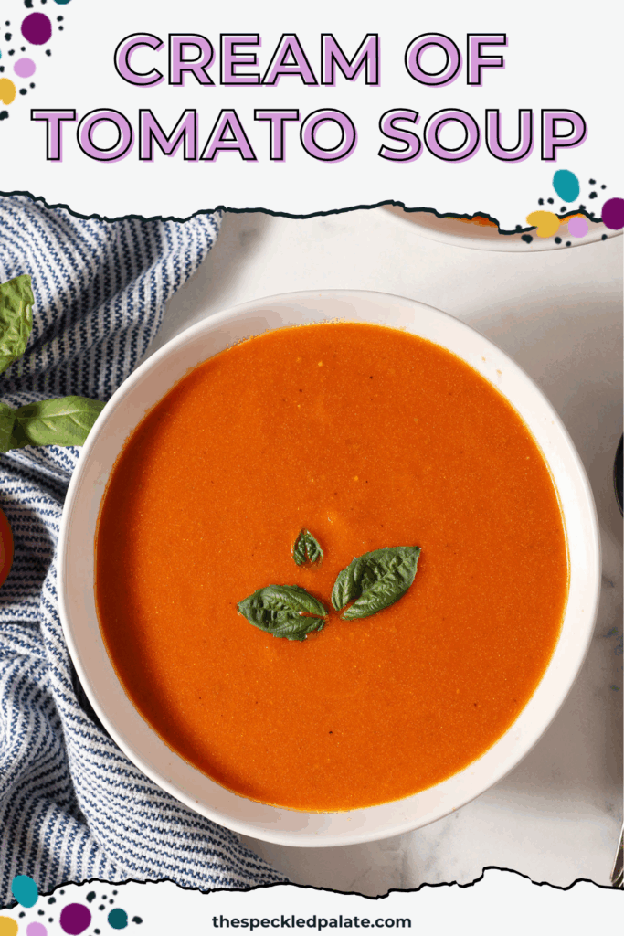 Close up of a bowl of fresh tomato soup with cream topped with fresh basil leaves on a marble surface next to a blue and white striped linen with the text cream of tomato soup