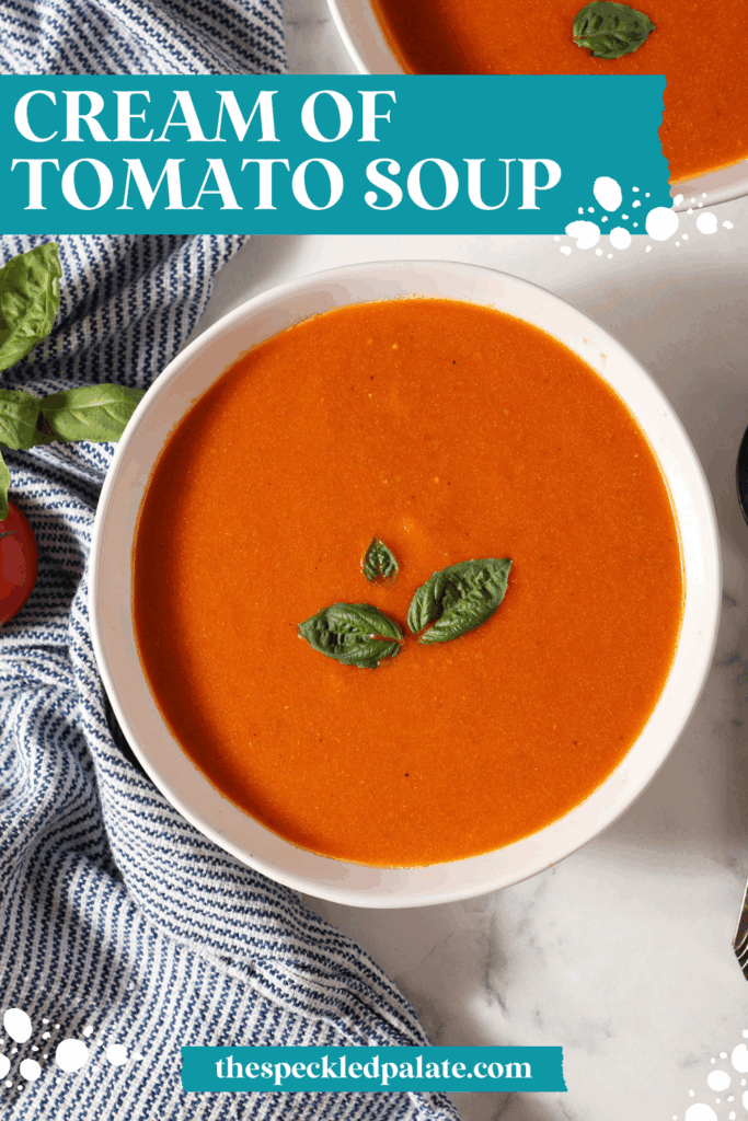 Close up of a bowl of fresh tomato soup with cream topped with fresh basil leaves on a marble surface next to a blue and white striped linen and another bowl with the text cream of tomato soup