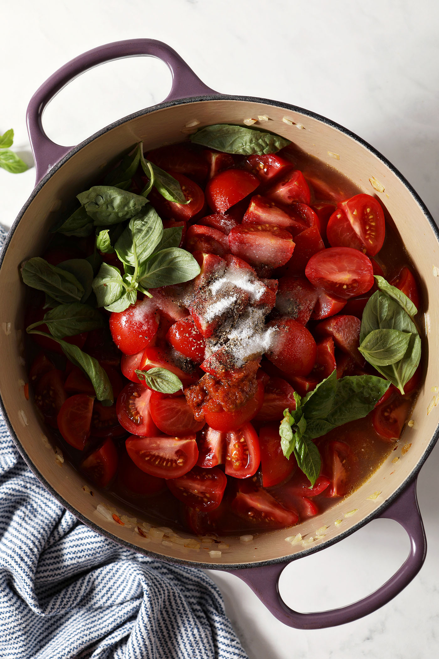 Fresh tomatoes, basil leaves, salt and more on top of a mirepoix in a dutch oven before cooking