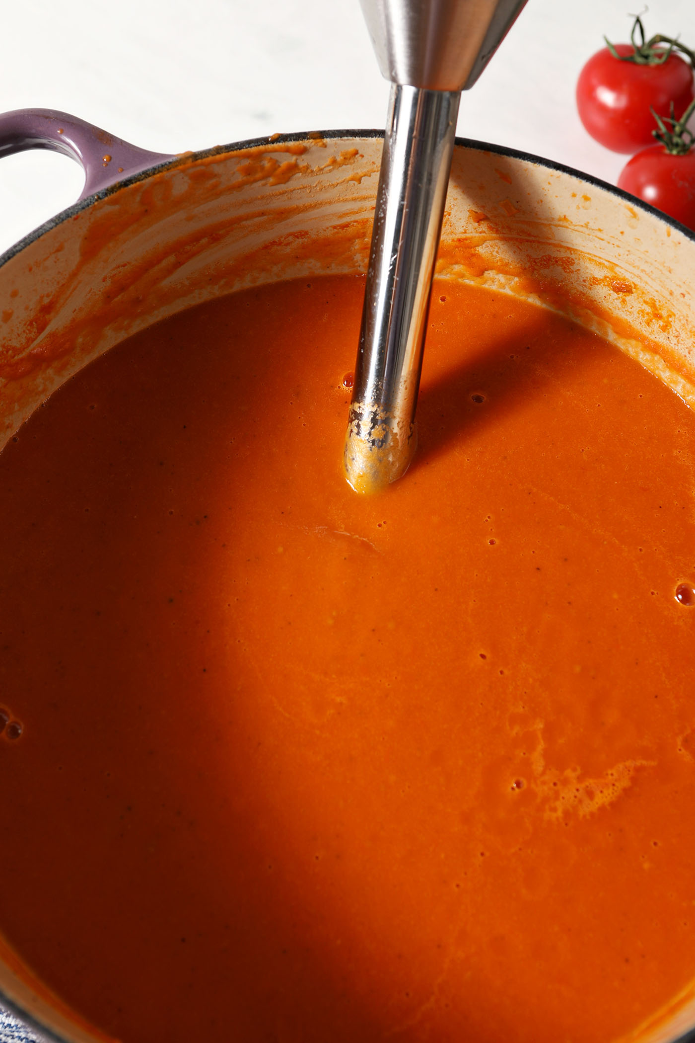 An immersion blender sits inside a dutch oven of fresh tomato soup