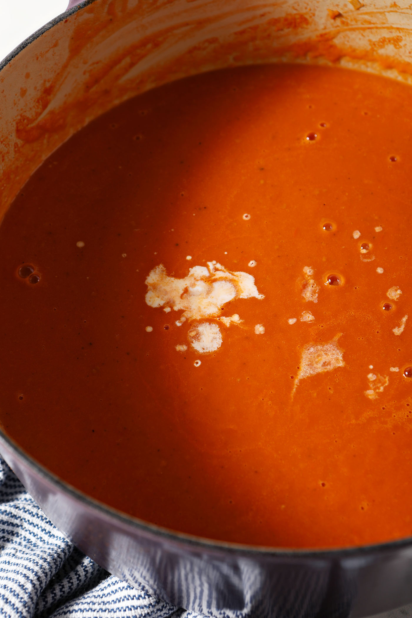 Cream sits on top of a dutch oven of fresh tomato soup before stirring