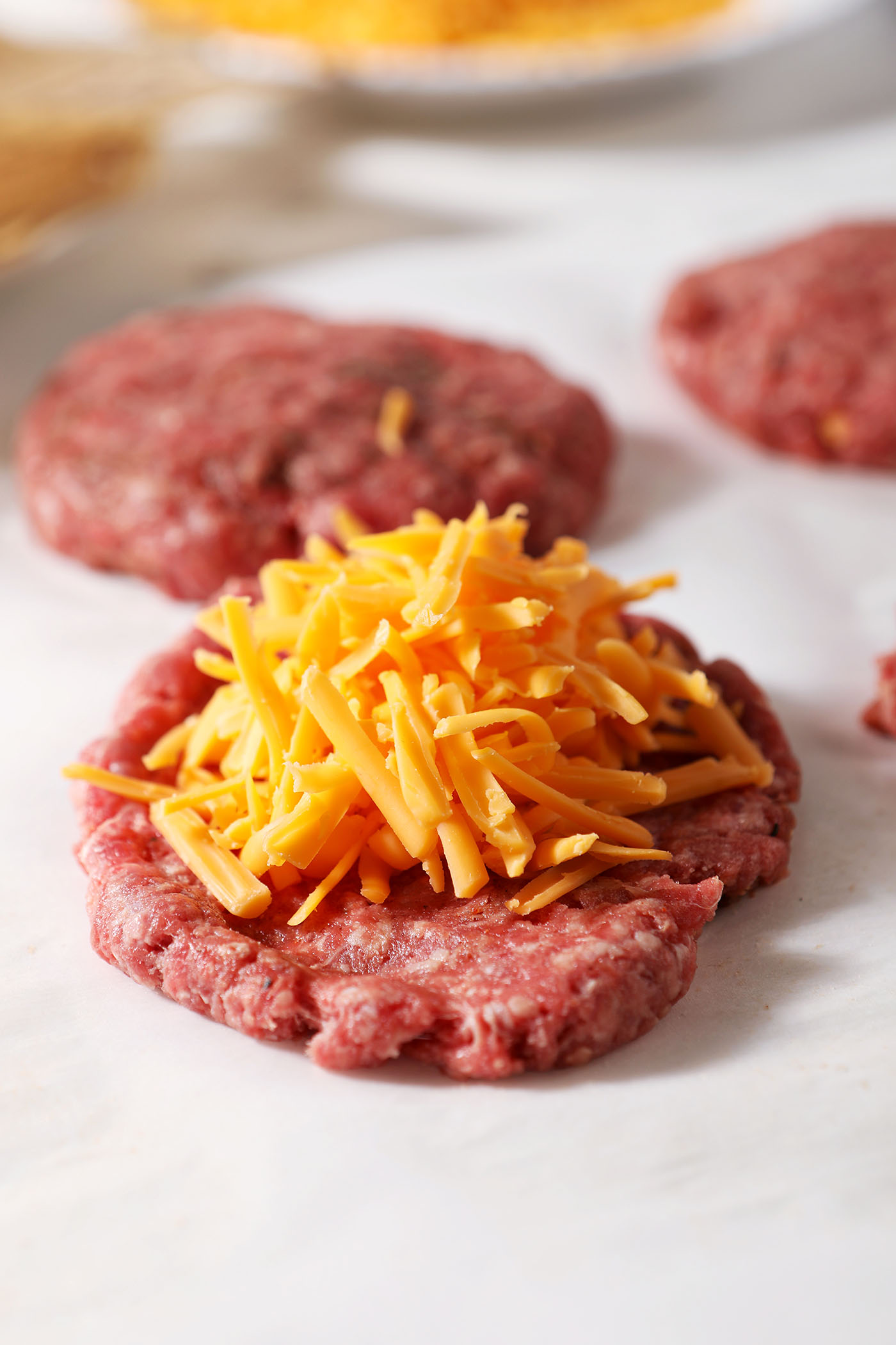 Shredded cheese on top of a thin burger patty before the rest of the meat is added