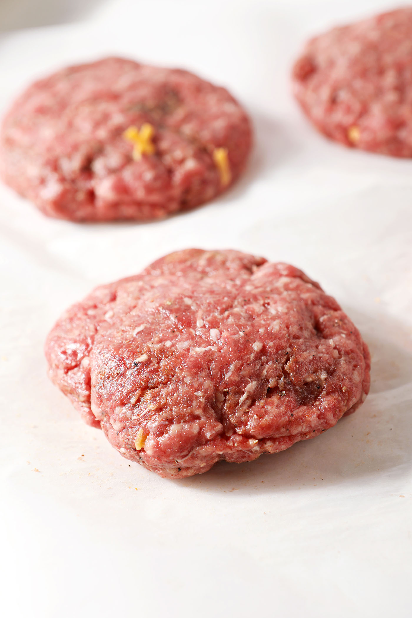 Juicy Lucy burger patties on parchment paper before grilling
