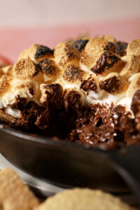 Close up of melty s’mores dip in a skillet with toasted marshmallows on top