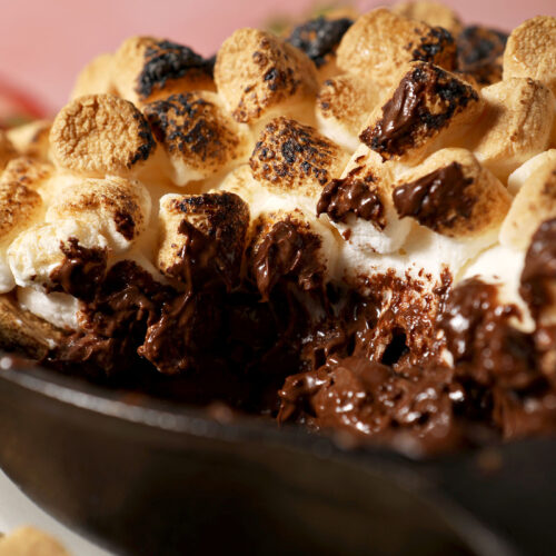 Close up of melty s’mores dip in a skillet with toasted marshmallows on top