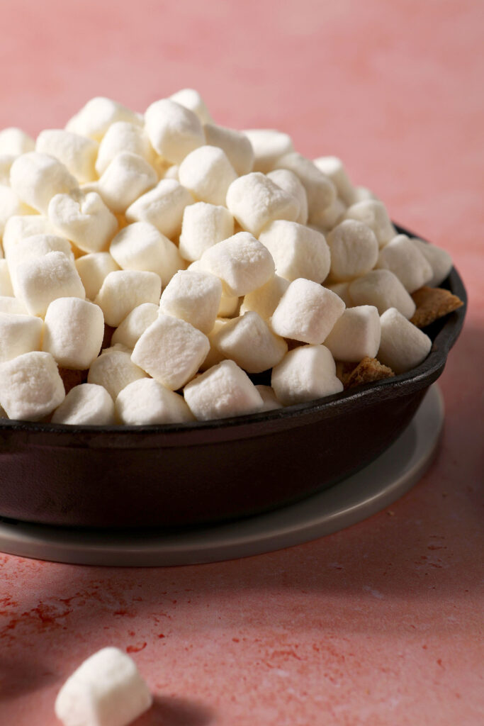 Marshmallows piled high in a skillet on a pink surface