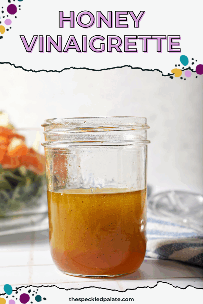 A jar of homemade honey vinaigrette in front of a salad on a white tiled surface with the text honey vinaigrette