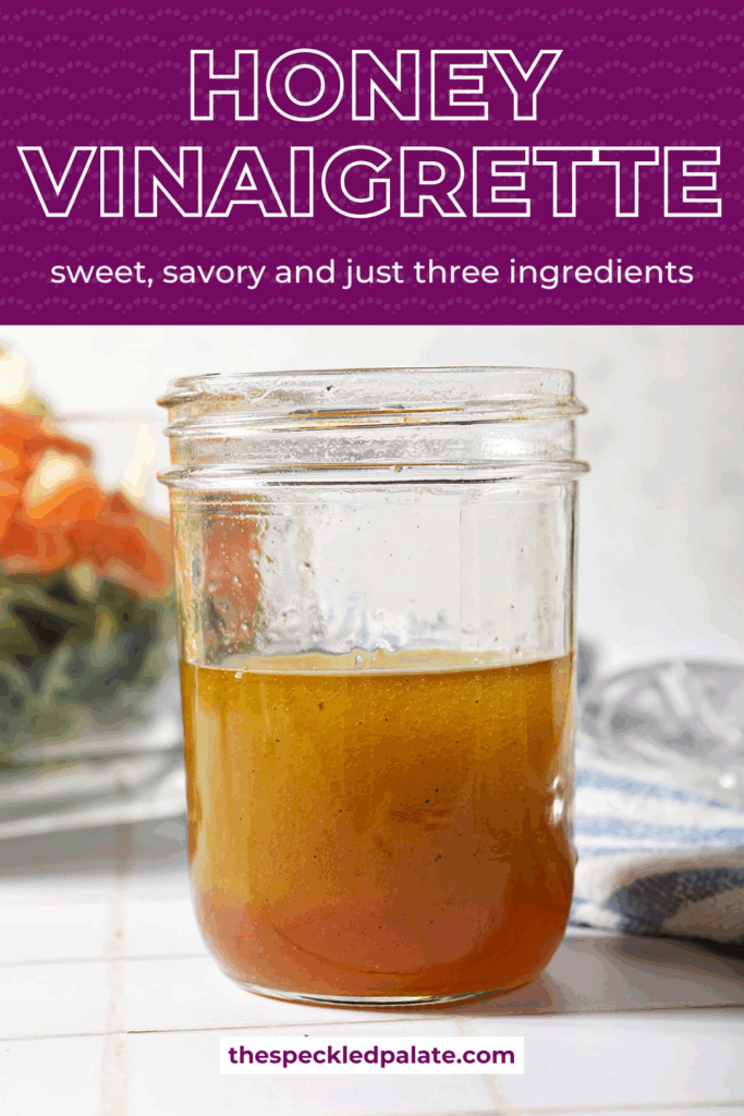 A jar of homemade honey vinaigrette in front of a salad on a white tiled surface with the text honey vinaigrette sweet, savory and just three ingredients