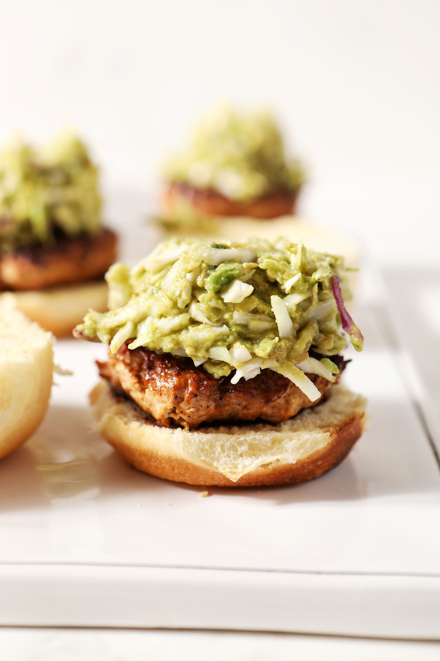 Avocado coleslaw on top of a bbq chicken burger on a white platter