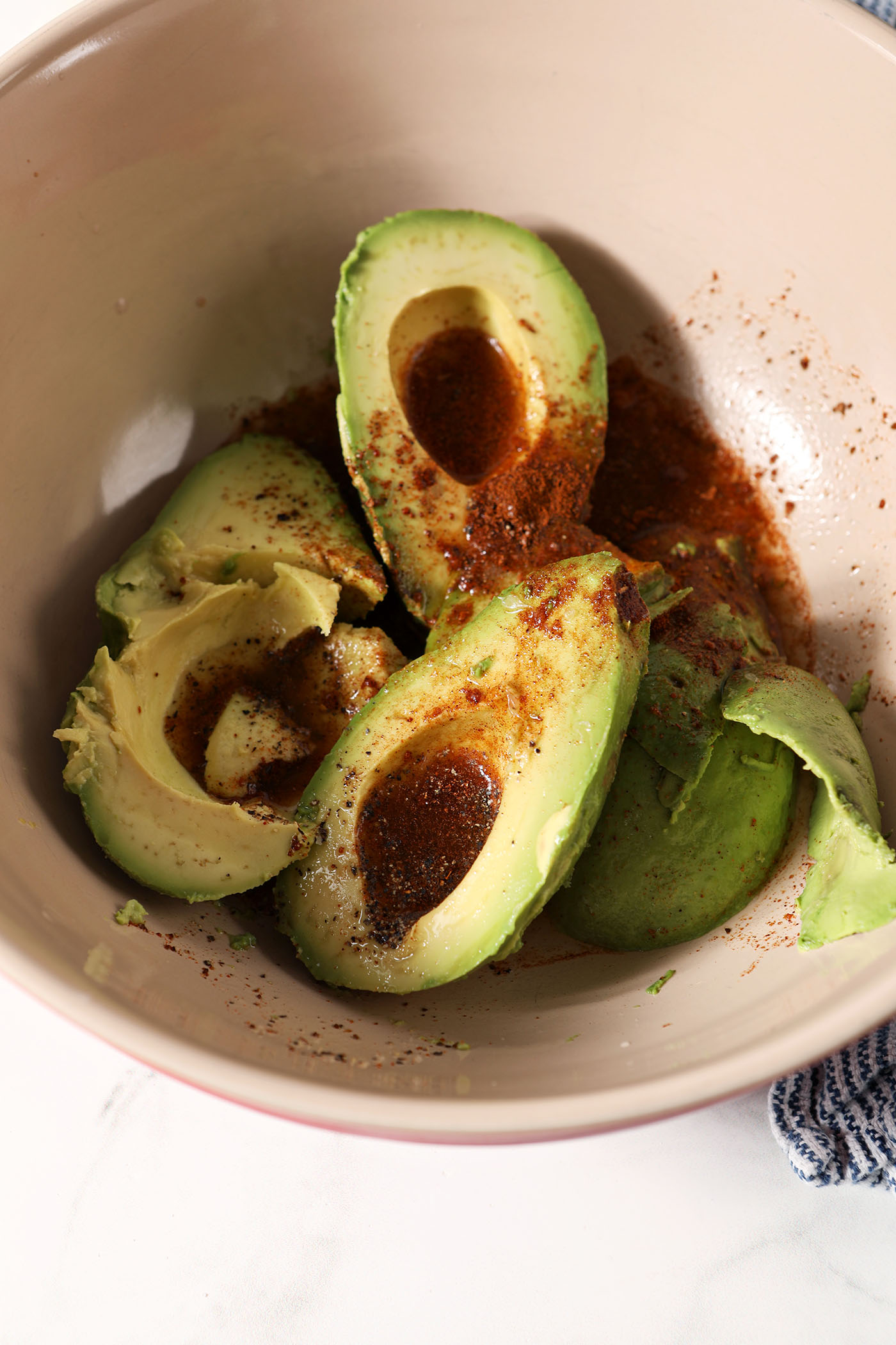 Halved avocados in a bowl seasoned with bbq seasoning