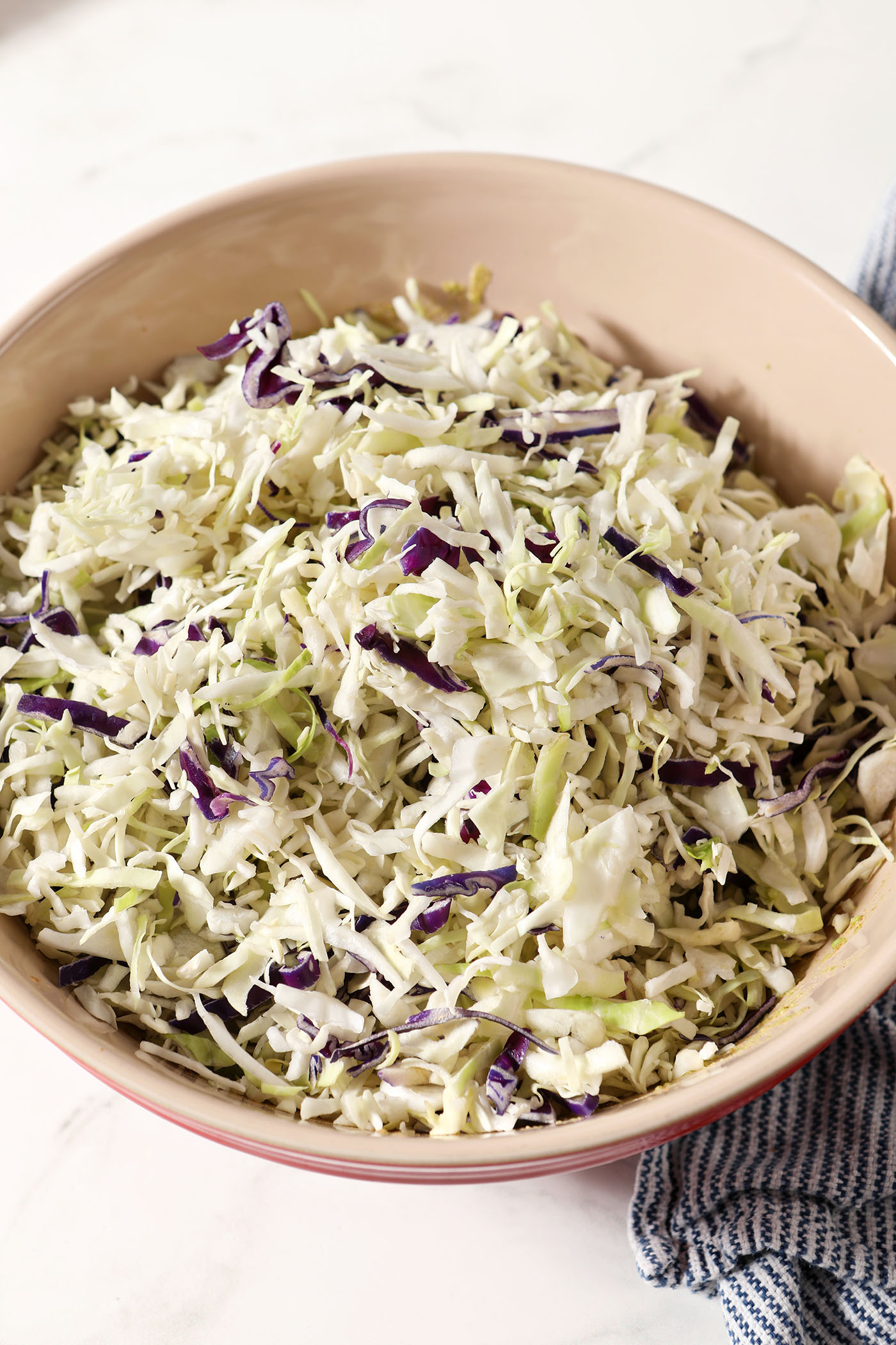 Shredded cabbage sits on top of smashed avocados in a bowl on a white surface