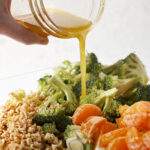 Honey vinaigrette pours on top of a salad with broccoli, oranges and ramen noodles