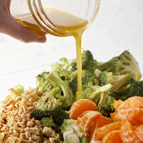 Honey vinaigrette pours on top of a salad with broccoli, oranges and ramen noodles