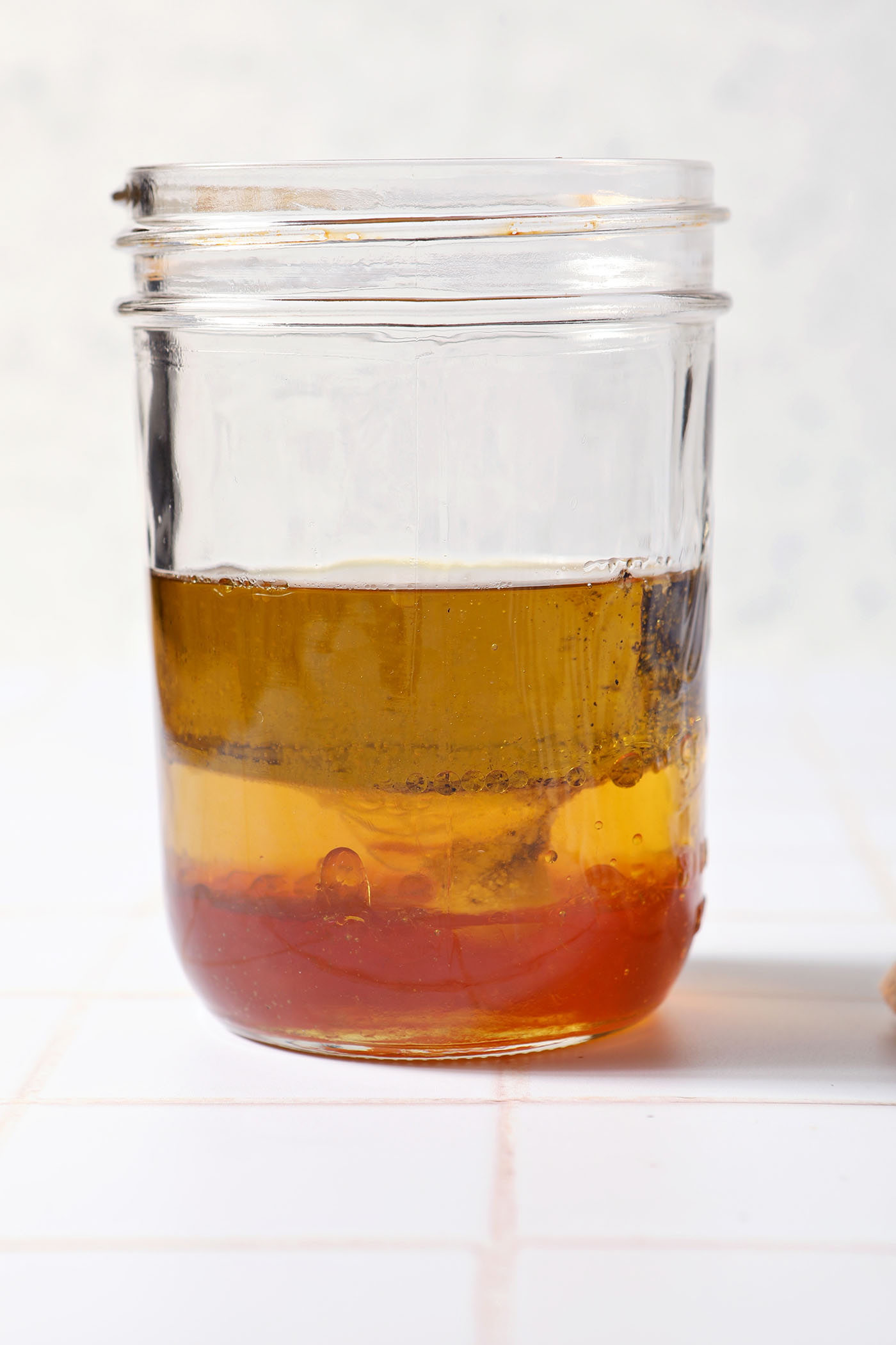 Ingredients to make a homemade honey salad dressing in a jar on a white tiled surface