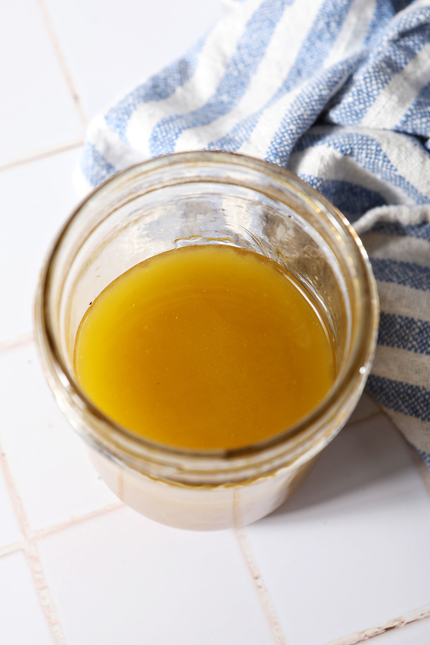 Mixed honey vinaigrette in a mason jar on a white tiled surface next to a blue and white striped linen