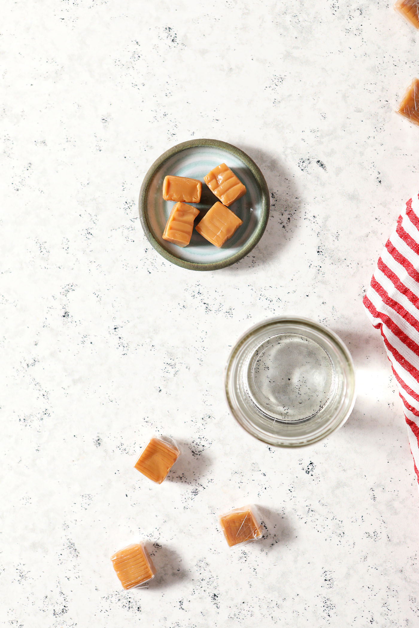 ingredients to make infused vodka with caramels on a white surface next to a white and red striped linen