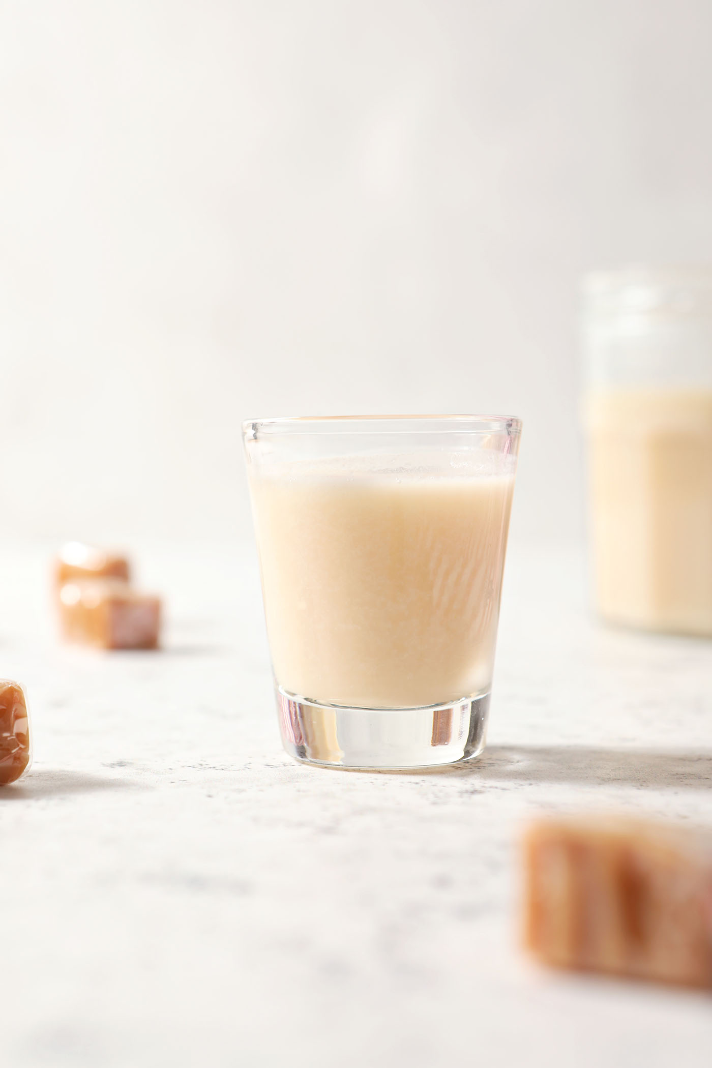 A shot glass of caramel infused vodka on a white surface surrounded by caramels