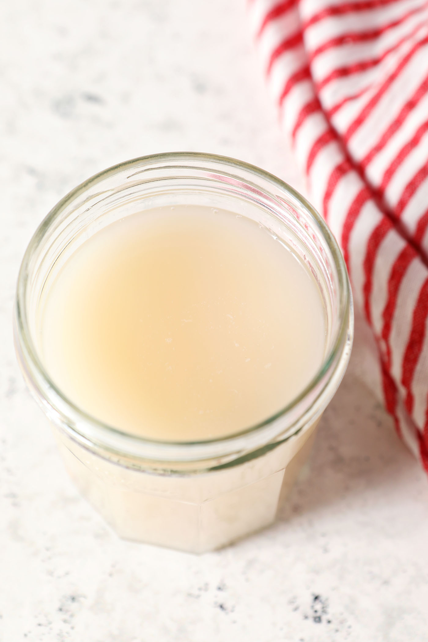 Close up of caramel vodka as it infuses in a jar next to a red and white striped linen