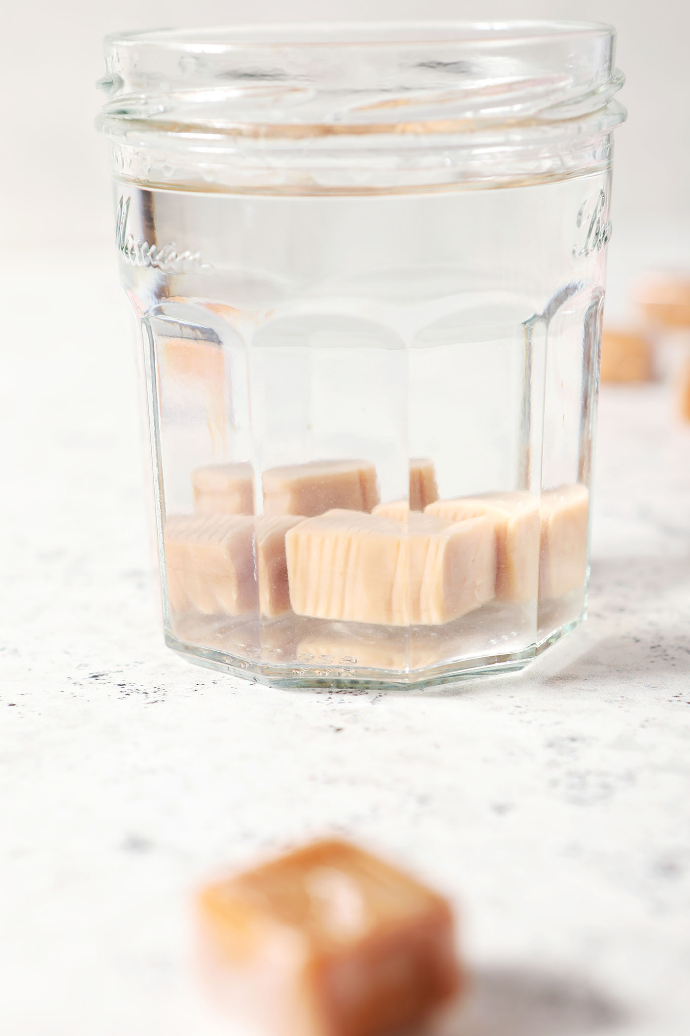 Caramels infuse into vodka in a glass jar on a white textured surface covered with soft caramels