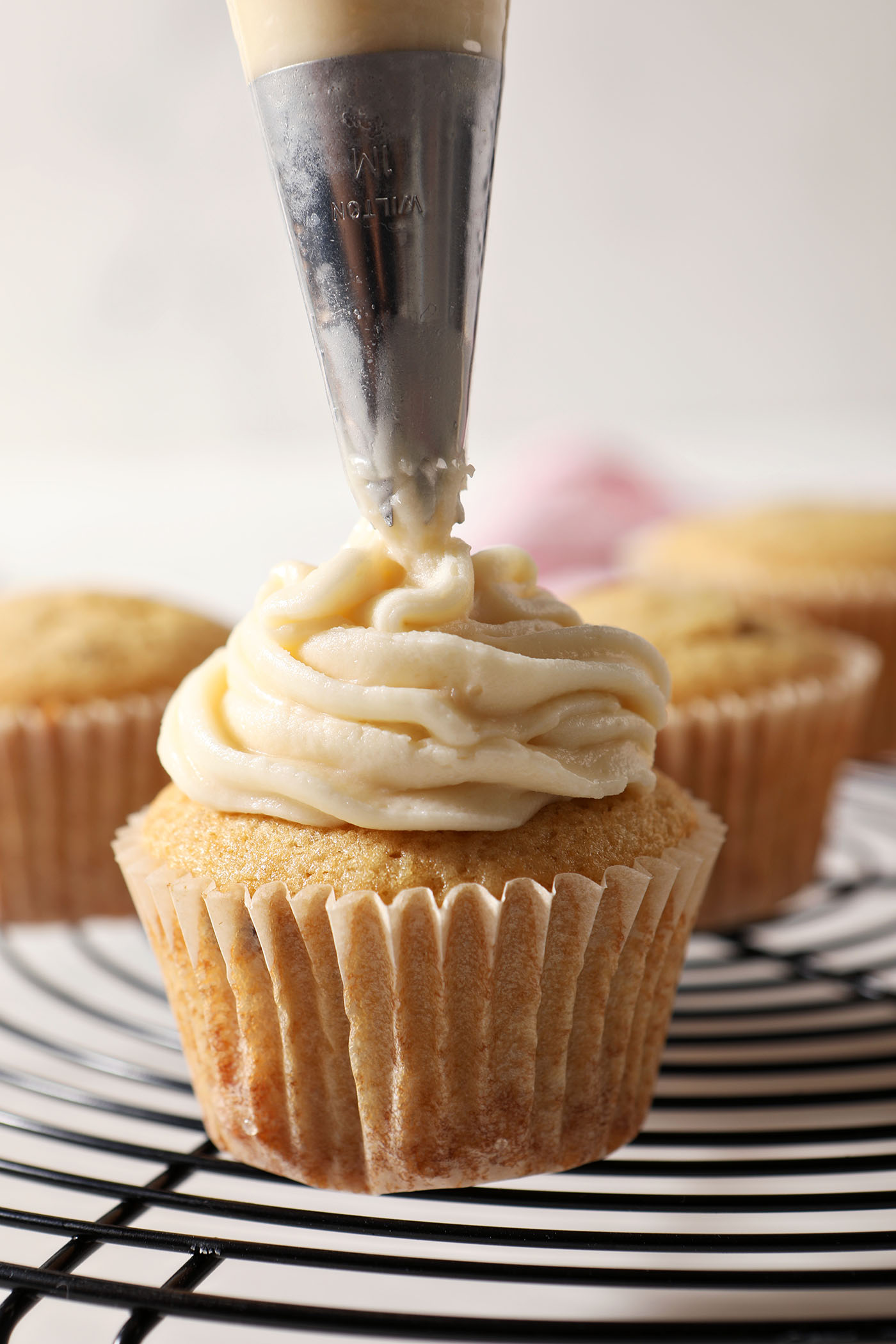 A cupcake is frosted with Salted Maple Frosting in a frosting bag on a cooling rack