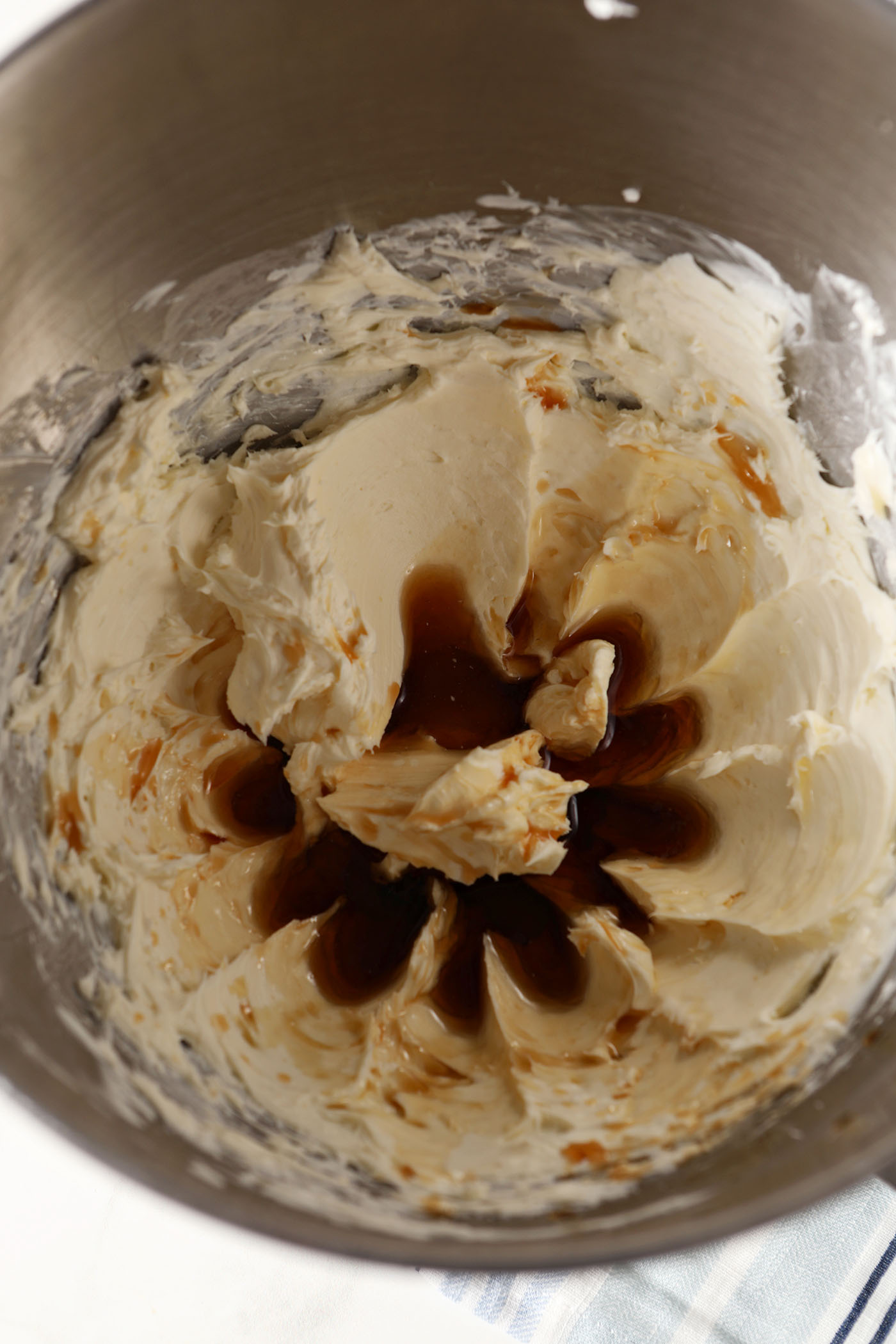 Maple and vanilla extract sit on top of creamed butter and cream cheese in a metal bowl