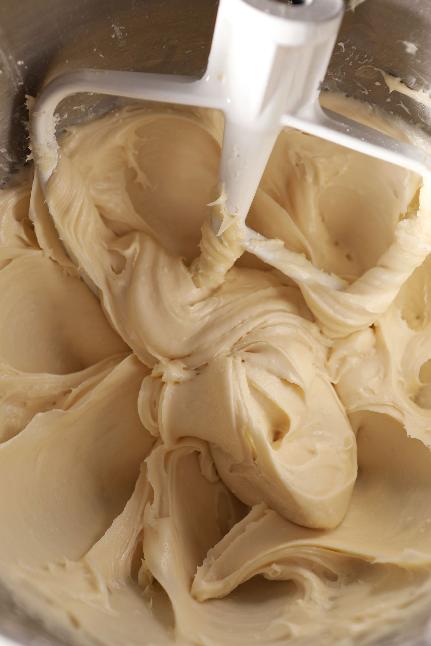 Close up of Salted Maple Frosting with a paddle attachment of a mixer in a metal bowl