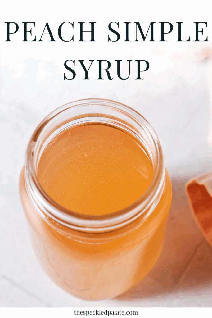 Overhead of a jar of peach syrup next to a peach and a pink linen on a grey tiled surface with the text peach simple syrup