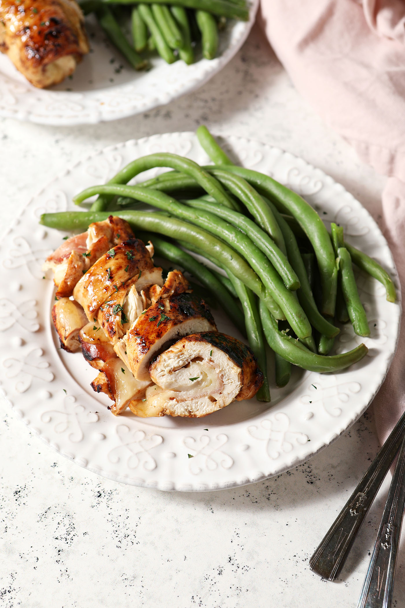A plate of sliced baked chicken cordon bleu next to green beans on a stone surface